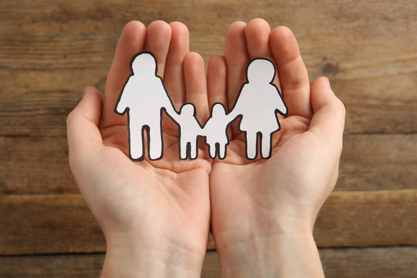 Woman holding paper family cutout on wooden background, closeup - Foto, afbeelding