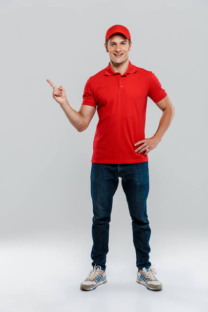 Young delivery man wearing uniform smiling and pointing finger aside isolated over white wall - Foto, afbeelding