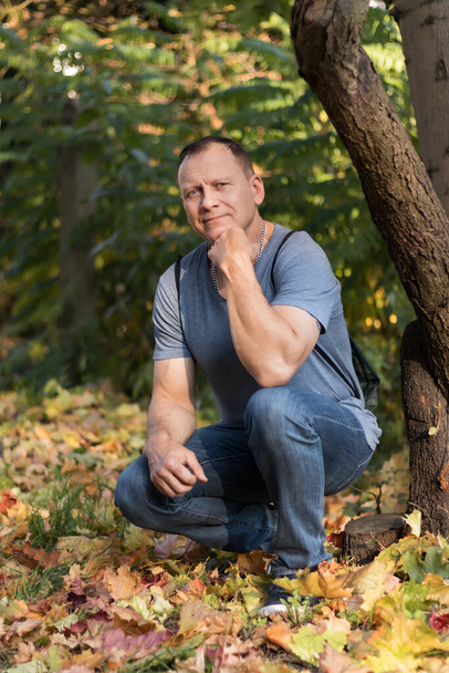 retrato de cuerpo entero de un hombre guapo y valiente con brazos musculosos, de 60 años, sobre el fondo de un bosque otoñal - Foto, imagen