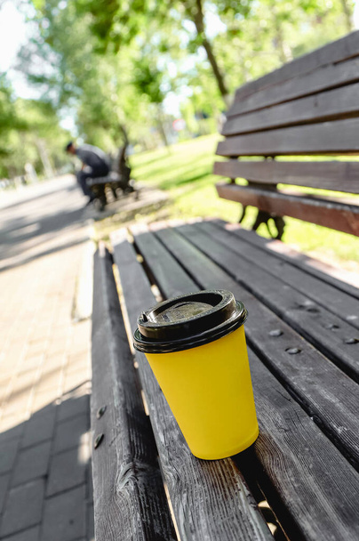 Güneşli bir günde parkta bankta sarı kağıt kahve fincanı. Açık havada yaz tatili. Seçici odaklı fotoğraf - Fotoğraf, Görsel