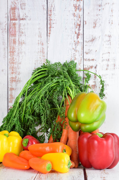 Assorted peppers and bunch of carrots on light colored rustic wood. Copy space. - Photo, Image