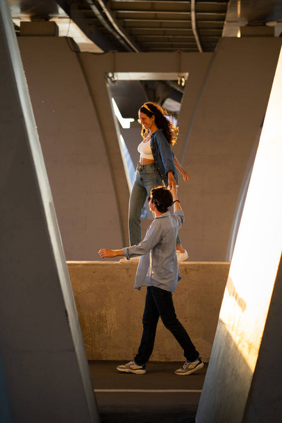 Trendy man and woman walk under bridge. Casual couple in street style clothes and trendy sunglasses - Photo, Image