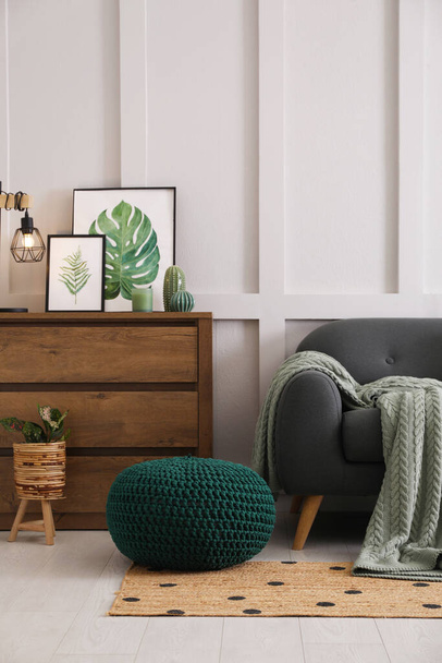 Stylish living room interior with knitted pouf, sofa and wooden chest of drawers - 写真・画像