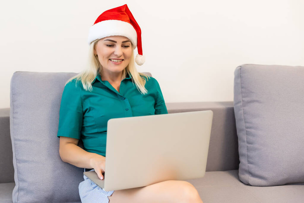 Una giovane donna sorridente con il cappello rosso di Babbo Natale che fa videochiamate sui social network con la famiglia e gli amici il giorno di Natale - Foto, immagini