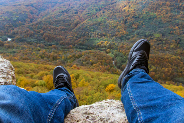 Ein Mann, der die malerische Aussicht bewundert, sitzt am Rande einer Klippe vor dem Hintergrund einer atemberaubenden Landschaft - Foto, Bild
