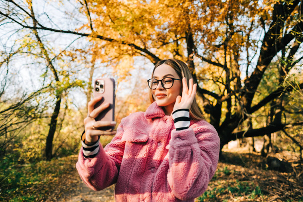 Young woman using smartphone in autumn park , heaving video call, communicate with friends or family. - Fotografie, Obrázek