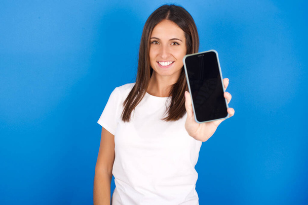 Encantadora adorable hermosa mujer joven sosteniendo un dispositivo moderno, mostrando el teléfono inteligente de pantalla negra - Foto, Imagen