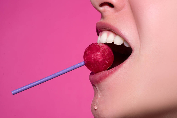 Closeup female lips with pink lipgloss holding in mouth red lollipop candy. Lollipop lips woman face. - Fotó, kép