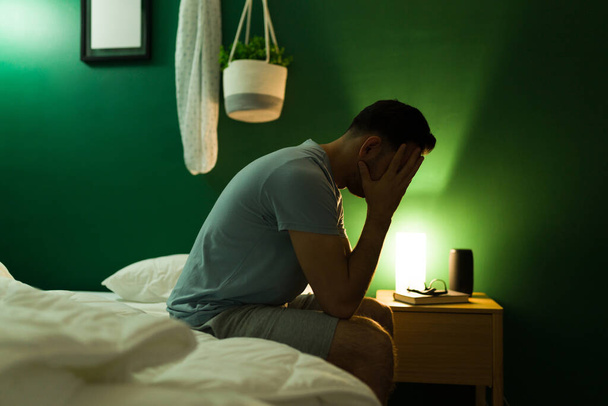 Hombre latino estresado cubriéndose la cara mientras se siente enfermo y deprimido en el dormitorio - Foto, imagen