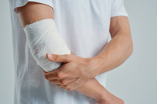 male patient in a white T-shirt with a bandaged hand light background - Foto, imagen