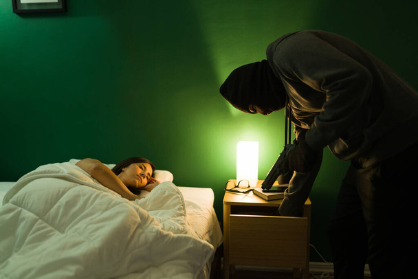 Burglar committing a crime and stealing valuable things inside a home at night while a woman alone is sleeping - 写真・画像