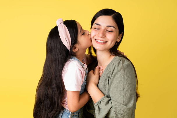 Adorabile bambina che bacia la sua bella madre sulla guancia e condivide i suoi sentimenti felici  - Foto, immagini