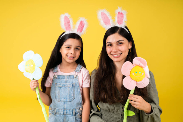 Porträt einer schönen Mutter und kleinen Tochter mit Hasenohren und Blumen zu Ostern  - Foto, Bild