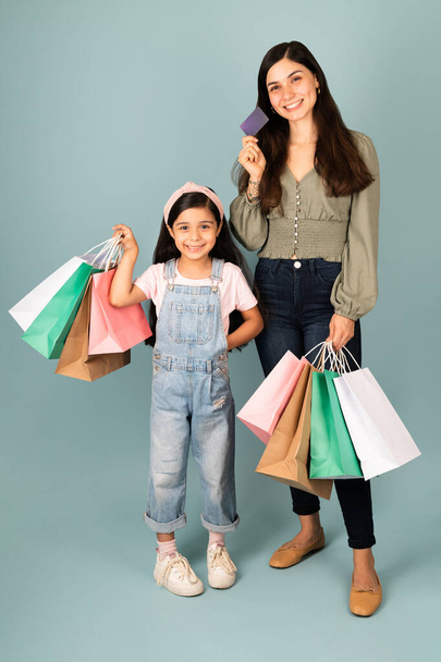 Atrakcyjna młoda kobieta płaci kartą kredytową z elementarną dziewczyną niosącą torby na zakupy  - Zdjęcie, obraz