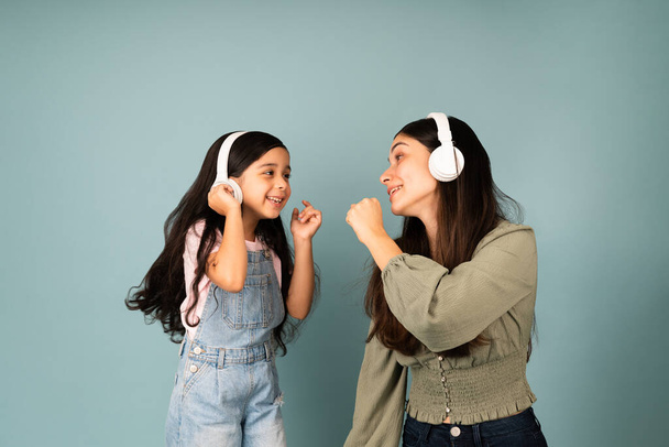 Sing with me. Hispanic young mom and little girl singing together while listening to music with headphones  - Foto, Imagen