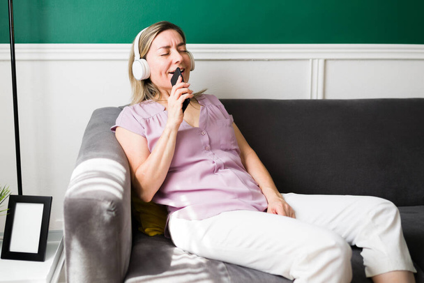 Fun senior woman home alone listening and singing her favorite song with wireless headphones  - Photo, Image