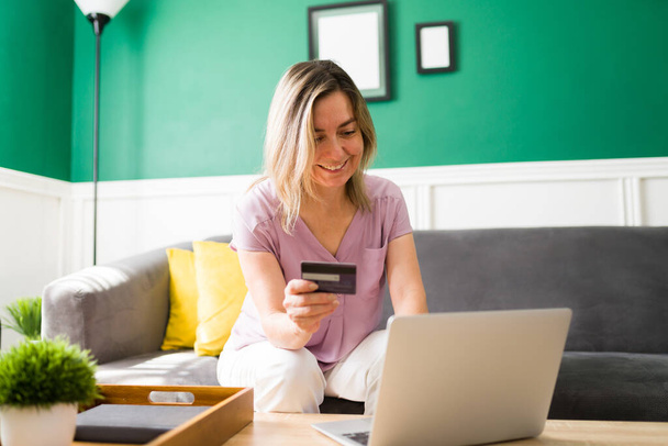 Χαρούμενη ώριμη γυναίκα πληκτρολογώντας στο laptop της και πληρώνοντας με πιστωτική κάρτα για online αγορές της  - Φωτογραφία, εικόνα