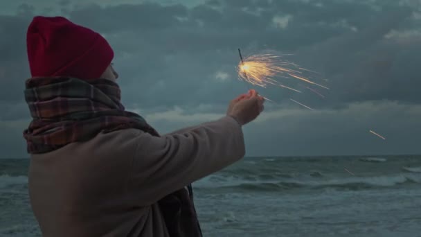 Γυναίκα στην ακτή του ωκεανού με πυροτεχνήματα λάμπει - Πλάνα, βίντεο