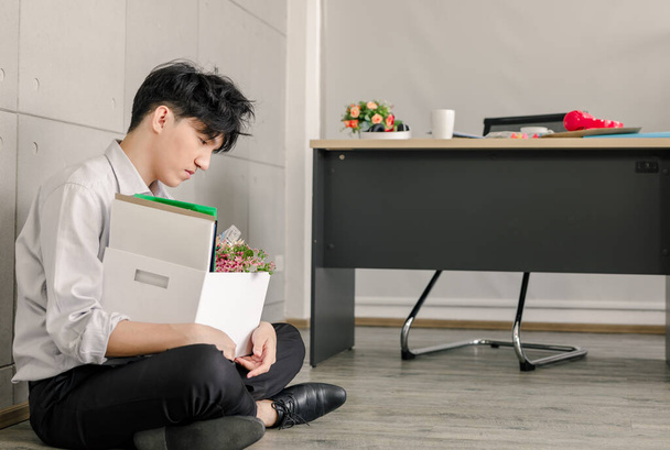 jonge aziatische zakenman zitten op de vloer in het kantoor en gestrest verdrietig na ontslagen uit zijn baan  - Foto, afbeelding
