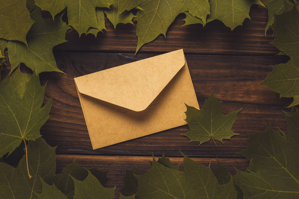 Une enveloppe postale fermée en feuilles d'érable sur fond de bois. Teintée. Humeur d'automne. Correspondance. - Photo, image