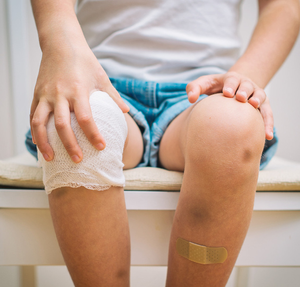 Child knee with adhesive bandage, bruise and gauze bandage. - Foto, Imagen
