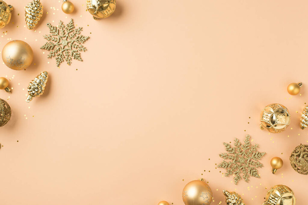 Top view photo of golden christmas tree decorations snowflakes cones balls and sequins in the corners on isolated beige background with copyspace - Photo, image
