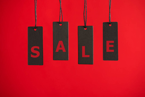Photo of hanging black price tags on isolated red background with text sale - Фото, зображення