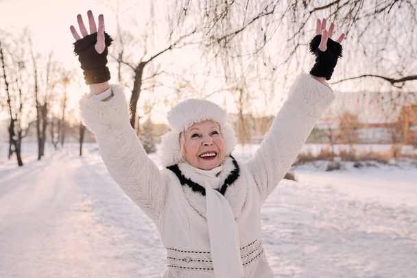 Végzős nő fehér kalapban és kabátban kocog a téli parkban. Tél, kor, évszak fogalma  - Fotó, kép