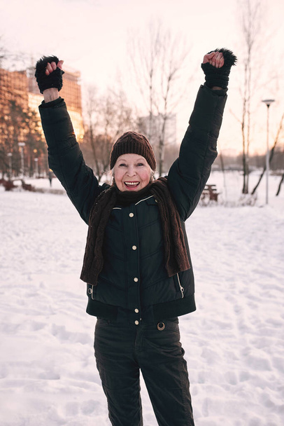 vanhempi nainen hattu ja urheilullinen takki lenkkeily lumi talvipuisto. Talvi, ikä, urheilu, toiminta, kauden käsite - Valokuva, kuva