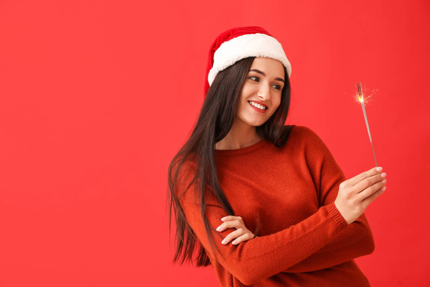 Young woman with Christmas sparkler on red background - Foto, Bild