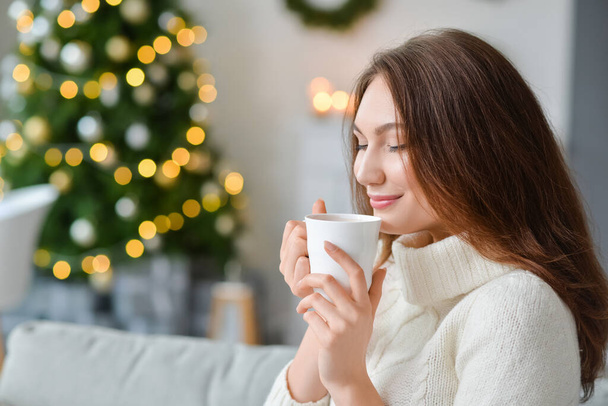 Όμορφη νεαρή γυναίκα με φλιτζάνι ζεστό κακάο ποτό στο σπίτι την παραμονή των Χριστουγέννων - Φωτογραφία, εικόνα
