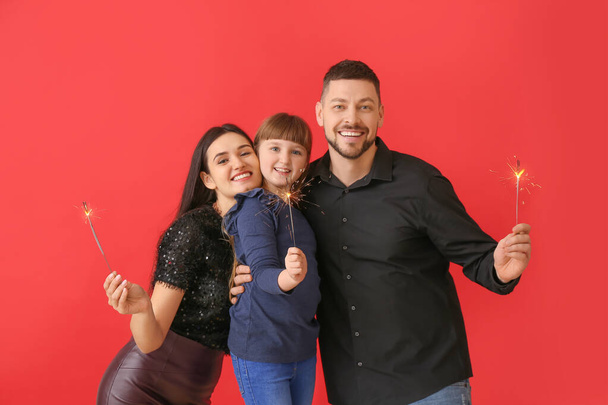 Happy family with Christmas sparklers on red background - Photo, Image