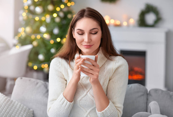 Beautiful young woman with cup of hot cacao drink at home on Christmas eve - Photo, Image