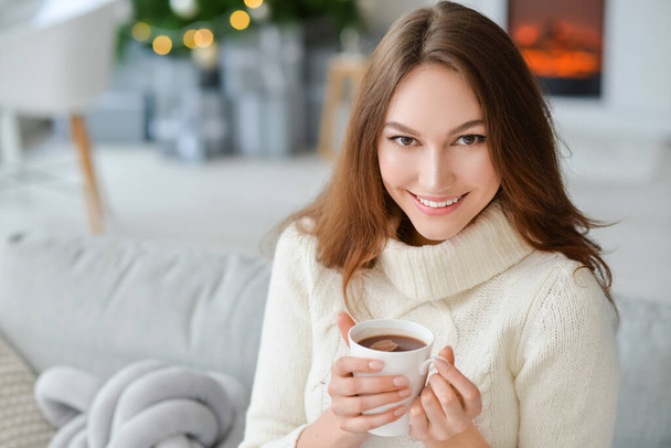 Beautiful young woman with cup of hot cacao drink at home on Christmas eve - 写真・画像