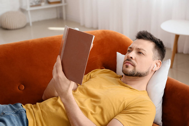 Uomo con auricolari e libro sdraiato sul divano - Foto, immagini