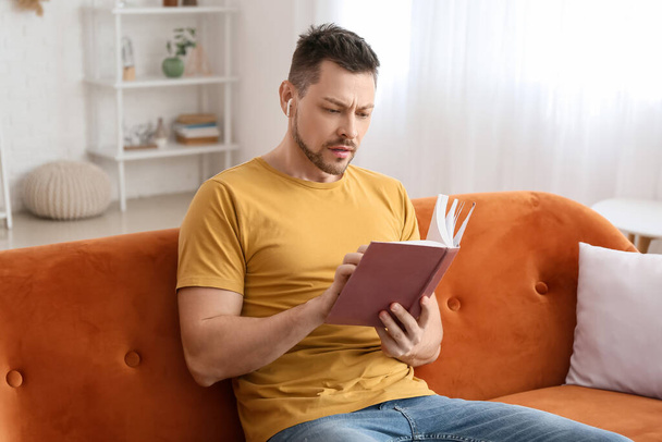 Férfi fülhallgatóval és könyv ül a kanapén - Fotó, kép