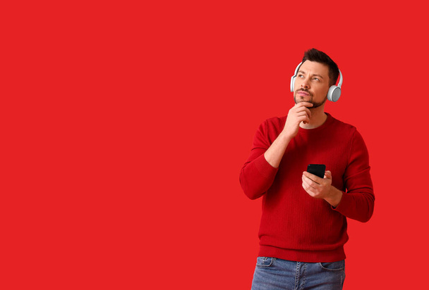 Thoughtful man with phone and headphones on color background - Φωτογραφία, εικόνα