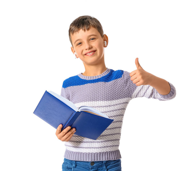 Malý chlapec s knihou a sluchátky ukazující palec nahoru na bílém pozadí - Fotografie, Obrázek
