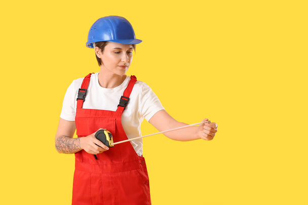 Trabajadora de construcción en hardhat con cinta métrica sobre fondo amarillo - Foto, Imagen