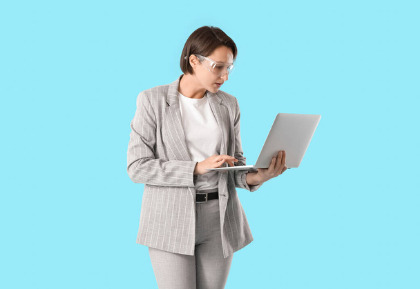 Ingegnere industriale femminile utilizzando laptop su sfondo blu - Foto, immagini