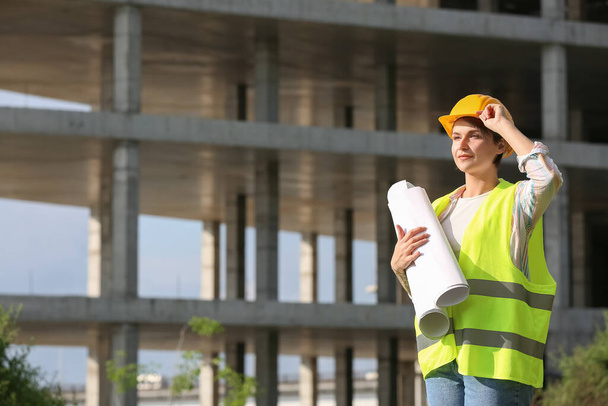 Naispuolinen rakennustyöntekijä kypärässä rullina paperia ulkona - Valokuva, kuva