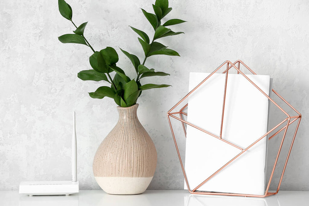 Modern wi-fi router, vase with branches and decor element on table near light wall - Foto, Imagem