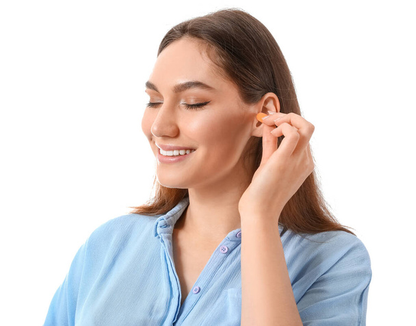 Young woman inserting earplugs on white background - Photo, Image