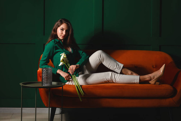 Красива молода жінка з квітами кали, сидячи на дивані біля кольорової стіни
 - Фото, зображення
