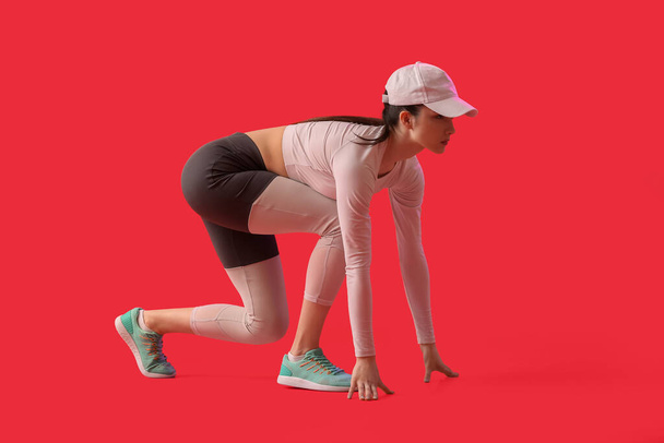 Sportieve jonge vrouw in crouch start positie op kleur achtergrond - Foto, afbeelding