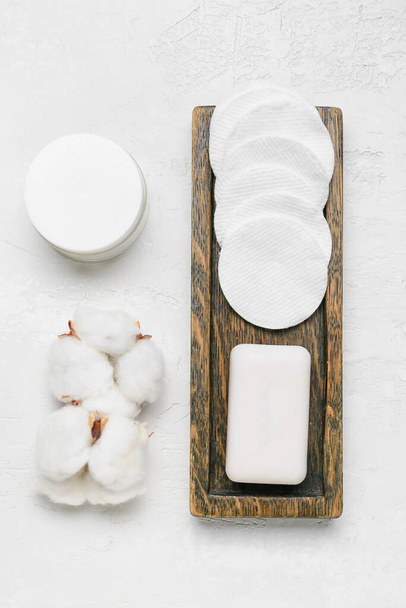 Board with cotton pads, flowers and cosmetic products on light background - Foto, Imagem