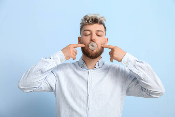 Grappige jongeman met kauwgom op kleur achtergrond - Foto, afbeelding