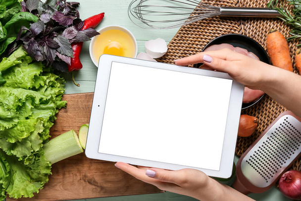 Woman holding digital recipe book and ingredients on color wooden table - Photo, Image