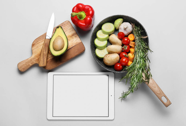 Digital recipe book, frying pan and wooden board with ingredients on white background - Photo, Image