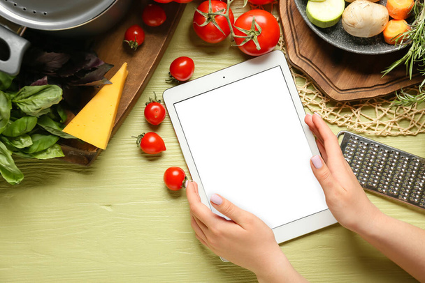 Manos femeninas con libro de recetas digital, ingredientes y utensilios de cocina sobre fondo de madera de color - Foto, imagen